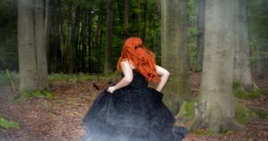 Frau mit rotem Haar läuft durch den Wald – Symbol für Lilith und innere Freiheit mit Titel "Lilith in den Zeichen"