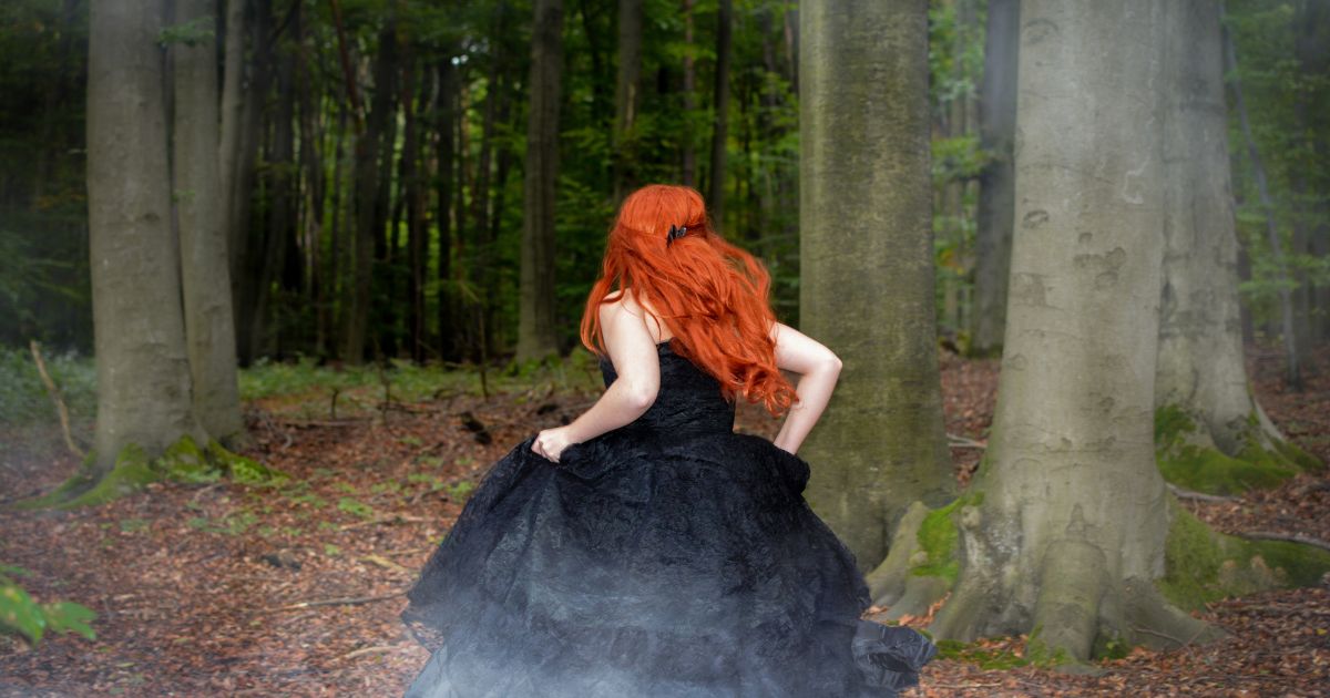 Frau mit rotem Haar läuft durch den Wald – Symbol für Lilith und innere Freiheit mit Titel "Lilith in den Zeichen"